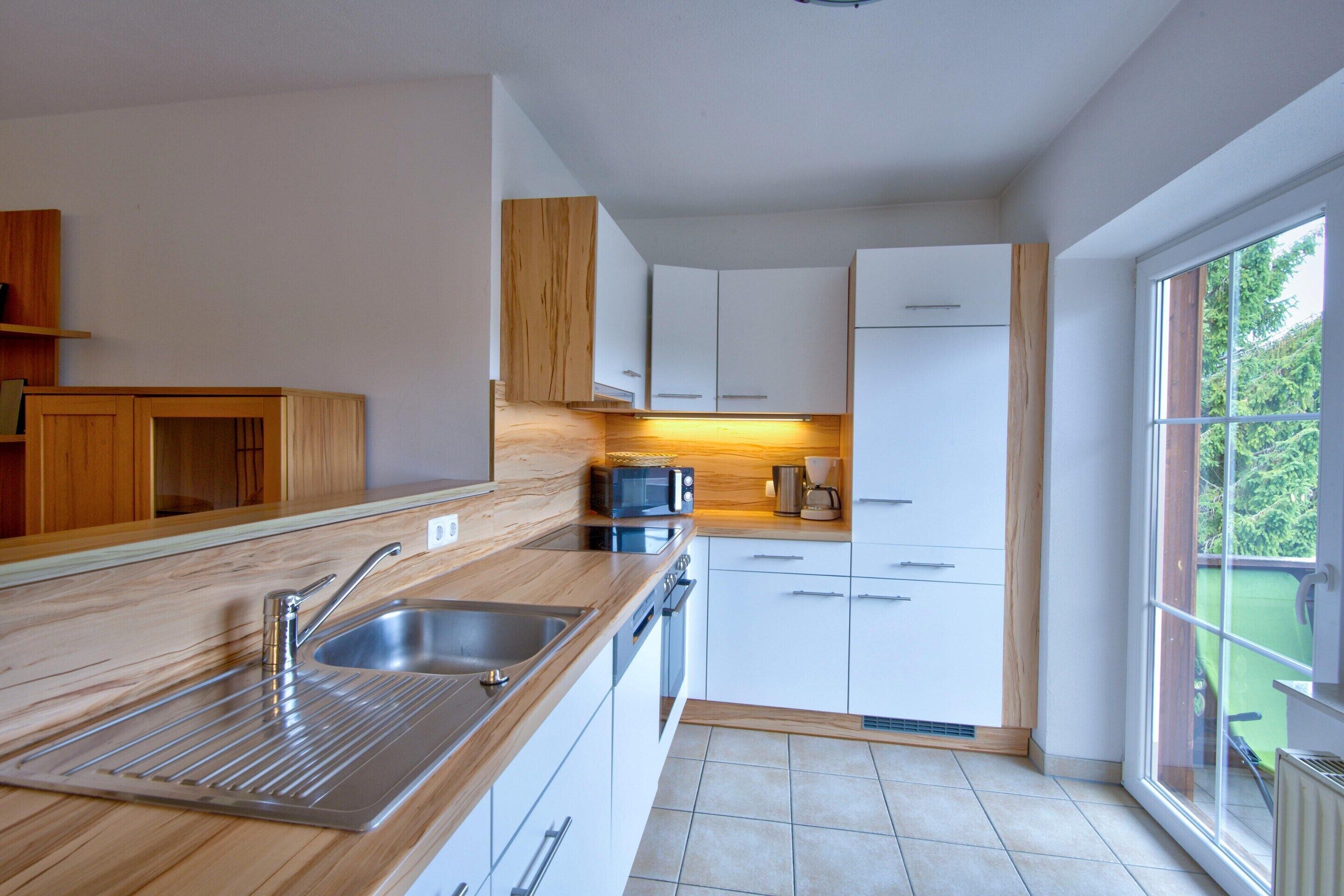 Een moderne keuken met een rvs spoelbak, een houten aanrechtblad, witte kastjes en een raam dat voor natuurlijk licht zorgt.