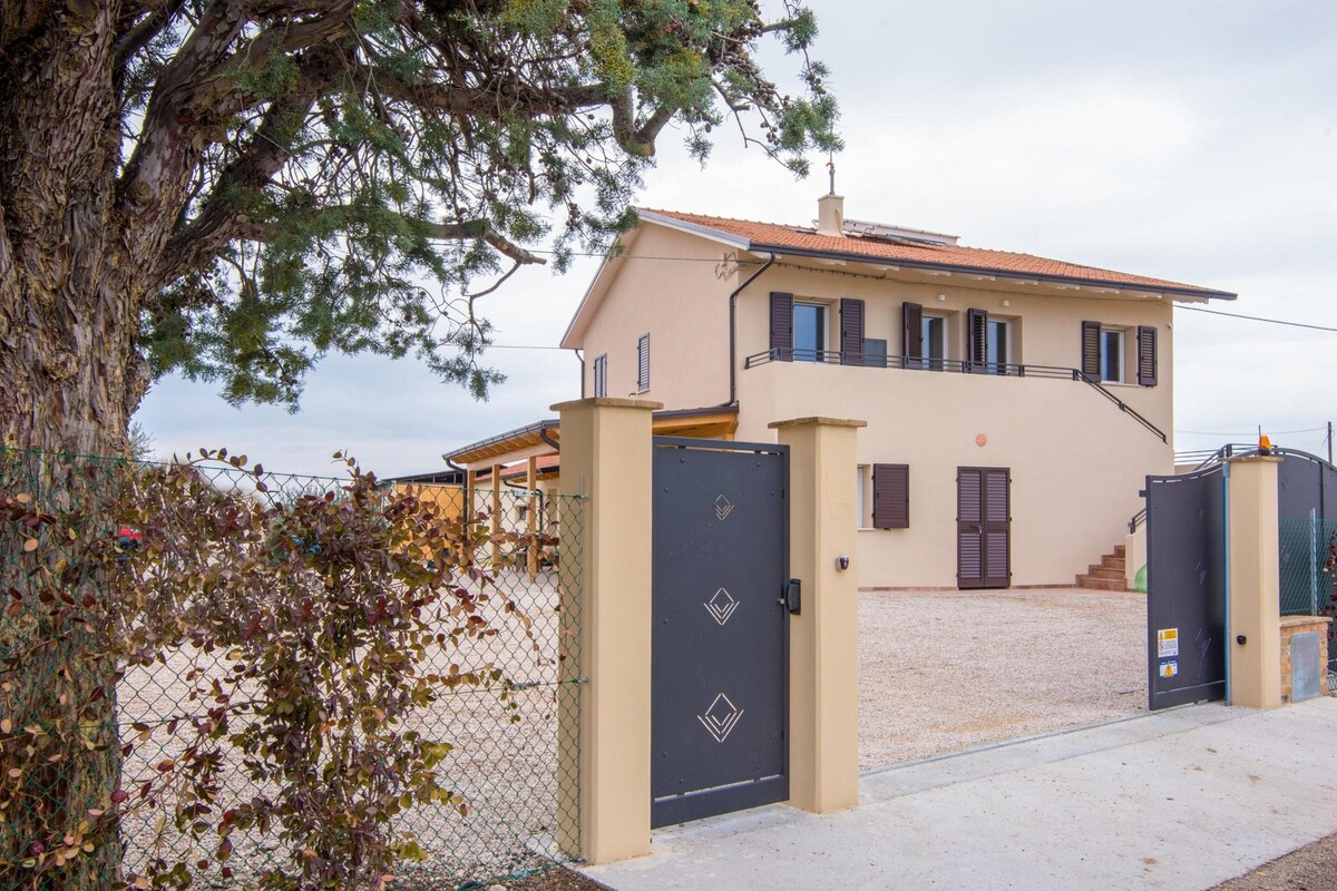 Una casa de dos pisos con fachada color beige, techo de tejas rojas y entrada protegida por una reja.