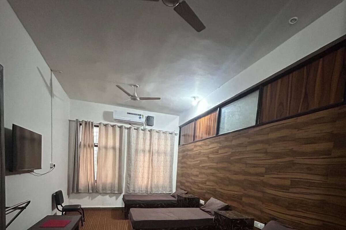 Ein Hotelzimmer mit zwei Betten, einem Fernseher, einem Deckenventilator und einem Fenster mit Vorhängen.