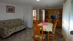 A dining area with a table and chairs, a sofa, and a kitchen in the background. - Nice Apartment With Garden (Oliva)