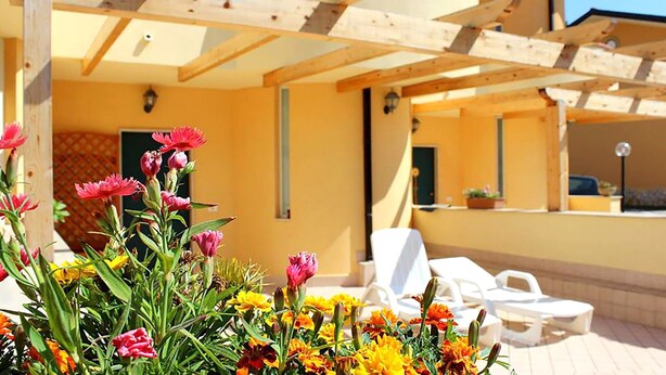 Un espace extérieur aménagé avec des sièges, protégé par un auvent, et un bâtiment jaune en arrière-plan.