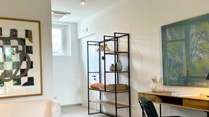 A modern living room with a white sofa, a black metal shelving unit, a wooden desk with a chair, and a large abstract painting on the wall. - A Casa Guesthouse (Mombaruzzo)