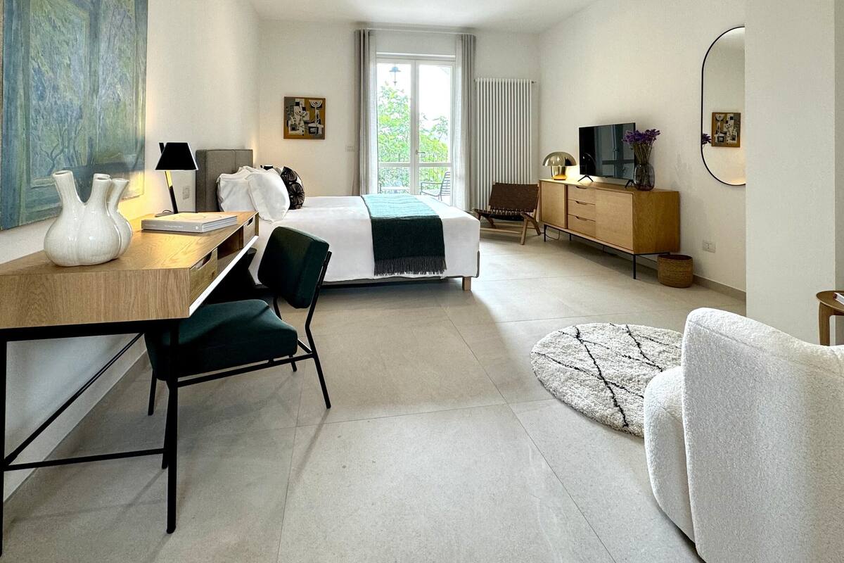 A modern hotel room with a bed, desk, chair, and a large window.