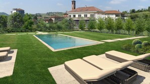 A swimming pool with lounge chairs, a well-manicured lawn, and a large house with a tower in the background. - A Casa Guesthouse (Mombaruzzo)