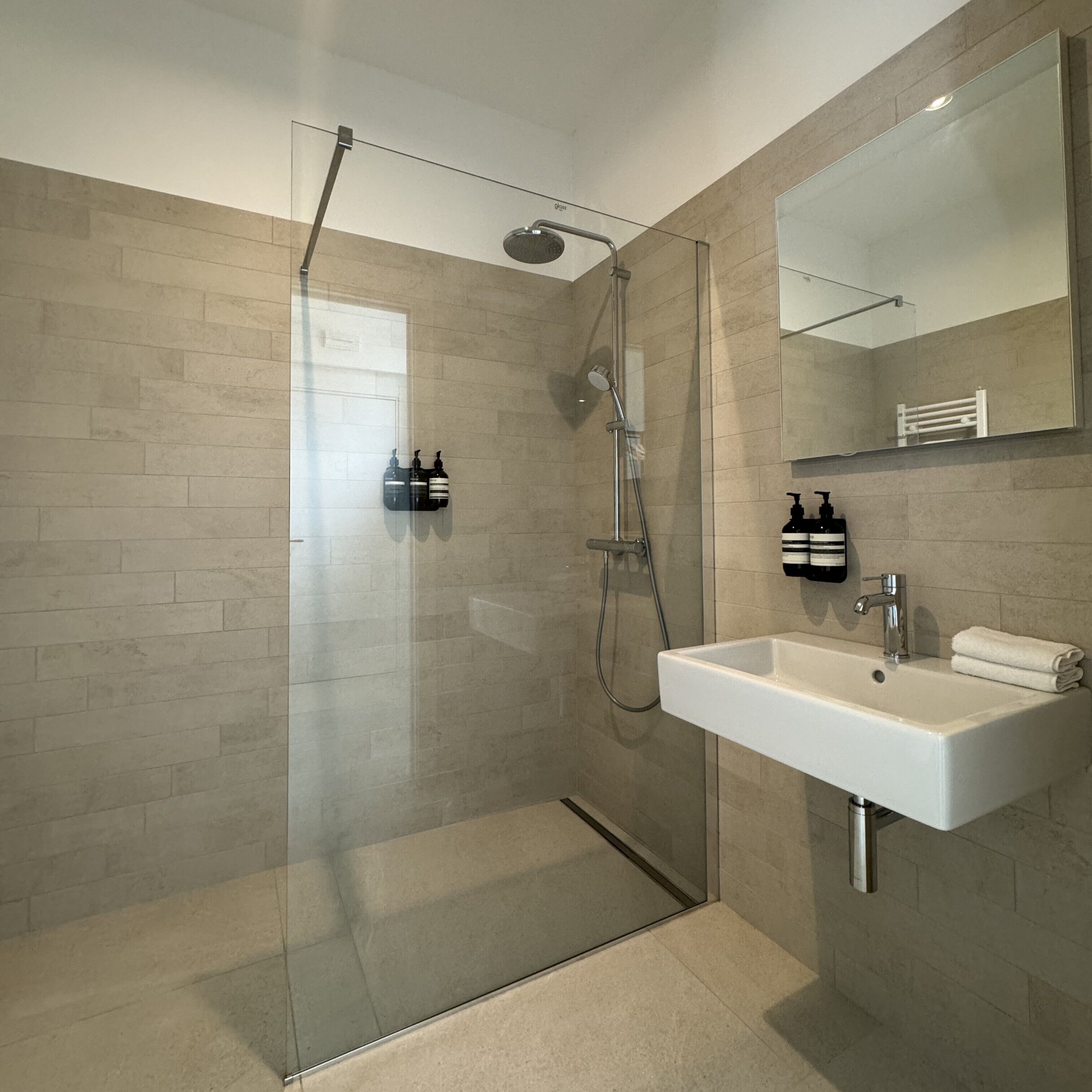Un bagno moderno con doccia vetrata, lavandino bianco e specchio sopra.