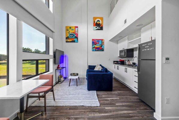 A modern kitchen with a dining area, large windows, and artwork on the walls.