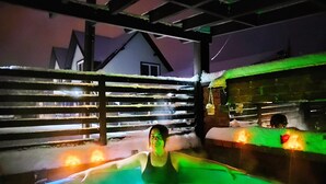 Una persona en un jacuzzi con una valla de madera y una estructura de ladrillo al fondo.