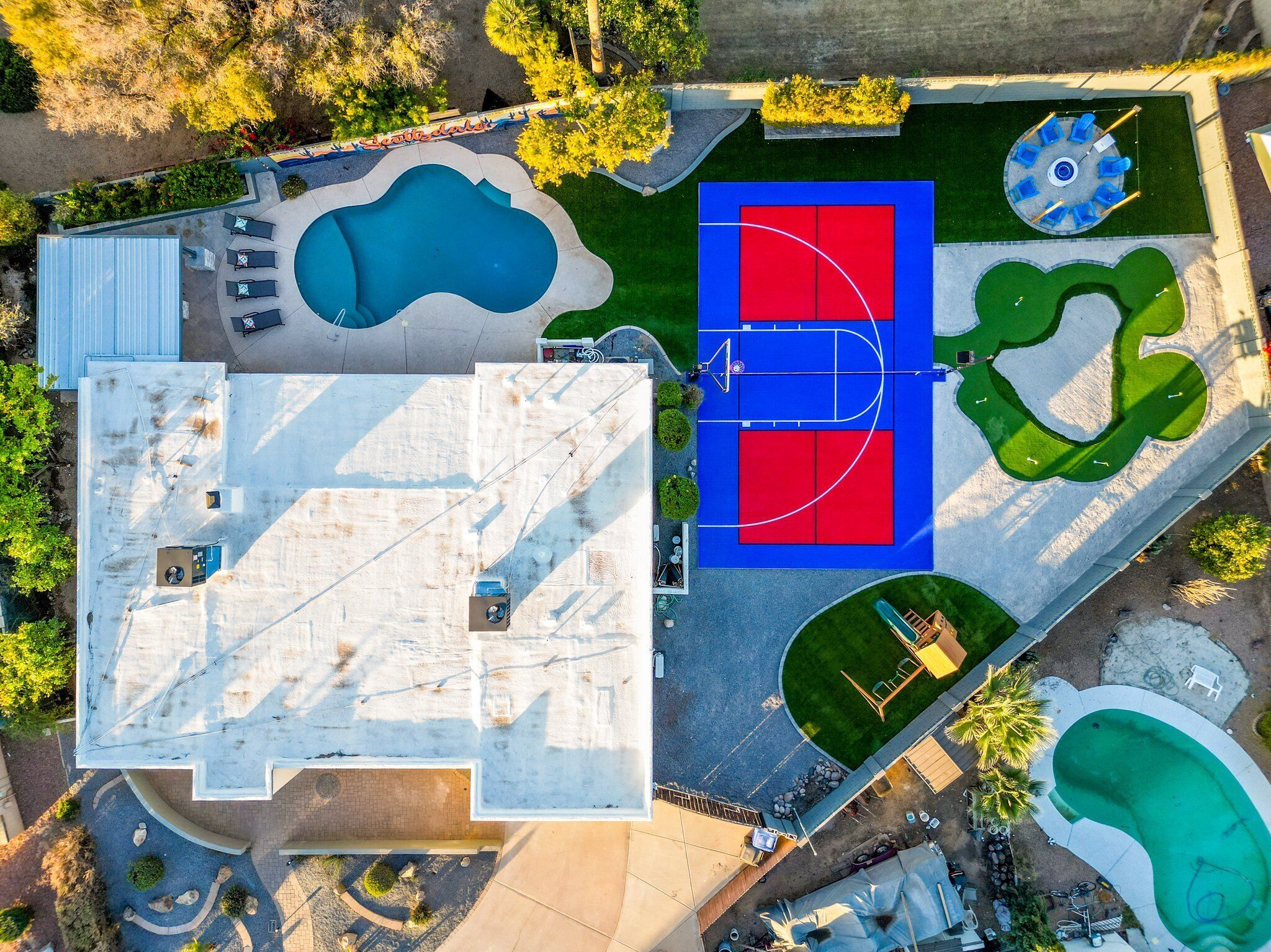 An aerial view of a property with a swimming pool, basketball court, and a tennis court.