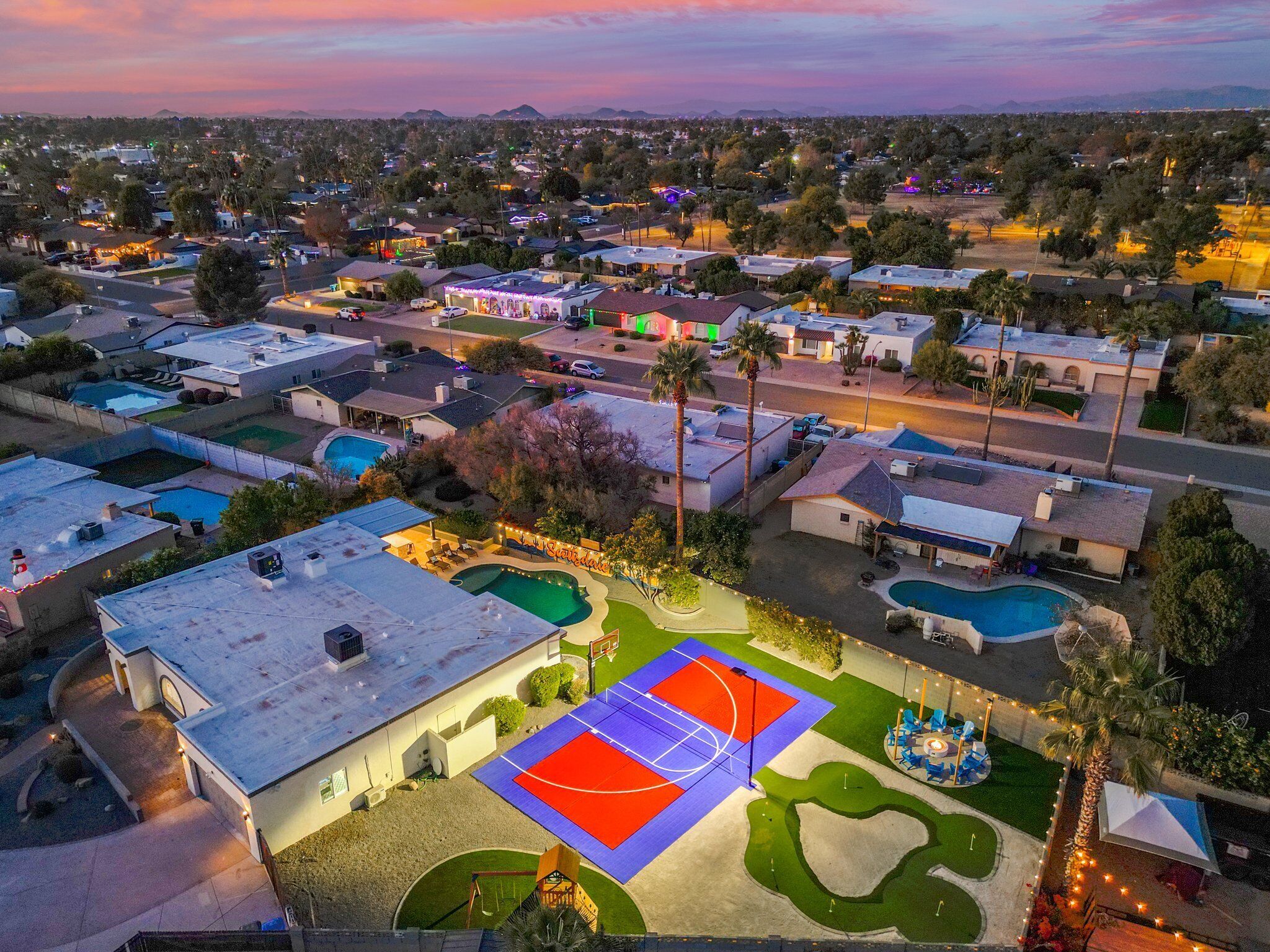 Vue aérienne d’un quartier résidentiel comprenant plusieurs maisons, un terrain de basket-ball et des piscines.
