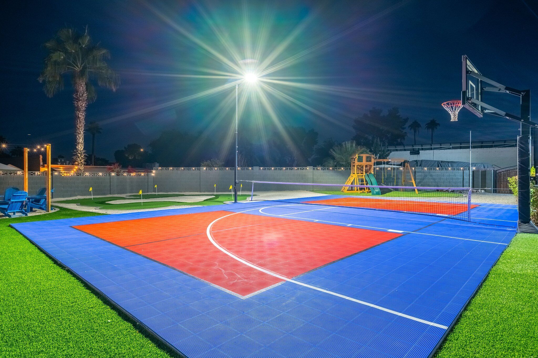 An outdoor basketball court with a net, a basketball hoop, and a brightly lit area.