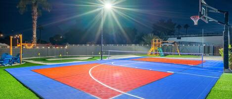 An outdoor basketball court with a net, a basketball hoop, and a brightly lit area.
