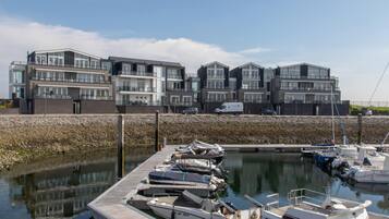 A marina with docked boats, a modern building with balconies, and a clear sky.