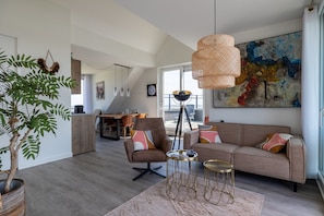 Un salon moderne avec un canapé, un fauteuil et un coin repas à l’arrière-plan.