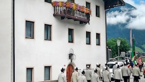 Un edificio con un balcón decorado con flores coloridas, una entrada tradicional y un cielo despejado con nubes.