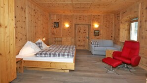 Una habitación de cabaña de madera con una cama, una silla roja, un sofá y dos lámparas de pared.