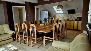 A dining area with a wooden table and chairs, a kitchen in the background, and a skylight above.
