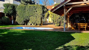 A backyard with a swimming pool, wooden deck, and a covered outdoor seating area.