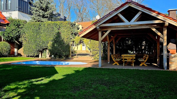 A covered outdoor seating area with a pool, surrounded by well-maintained grass and trees. - Comfortable House With Private Pool, Kolczewo (gmina Wolin)