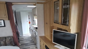 Cocina compacta con televisión, armarios de madera y una zona de comedor con mesa.