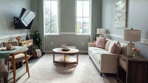 A living room with a TV mounted on the wall, a sofa, a coffee table, and a lamp. - Sanctuary Co Loft in Downtown Johnson City (Johnson City)