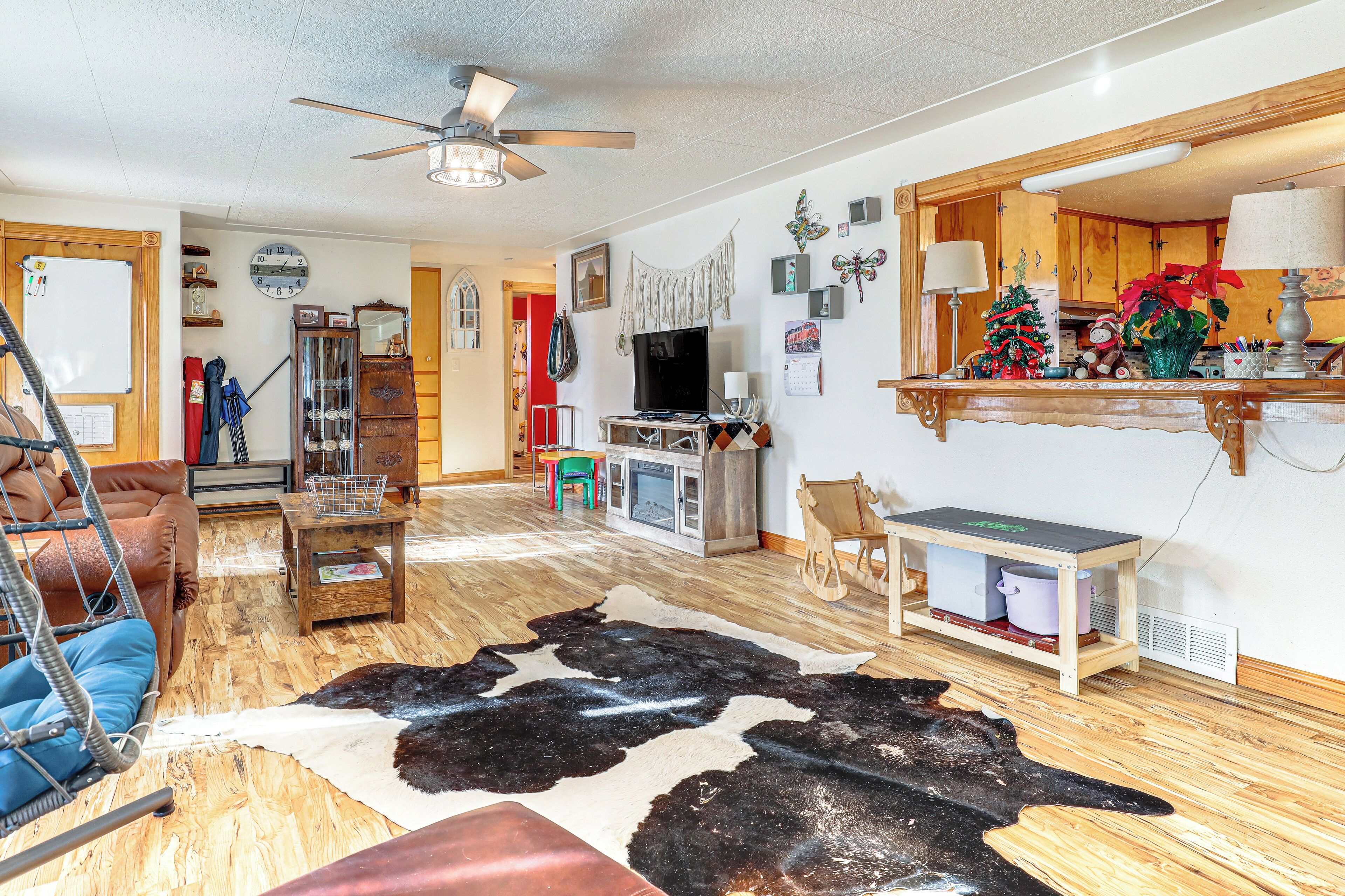 Un salon avec un plancher en bois, un tapis en peau de vache, un téléviseur, un meuble en bois et un sapin de Noël.