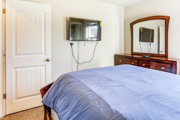 A bedroom with a bed, a television mounted on the wall, a dresser, and a door.