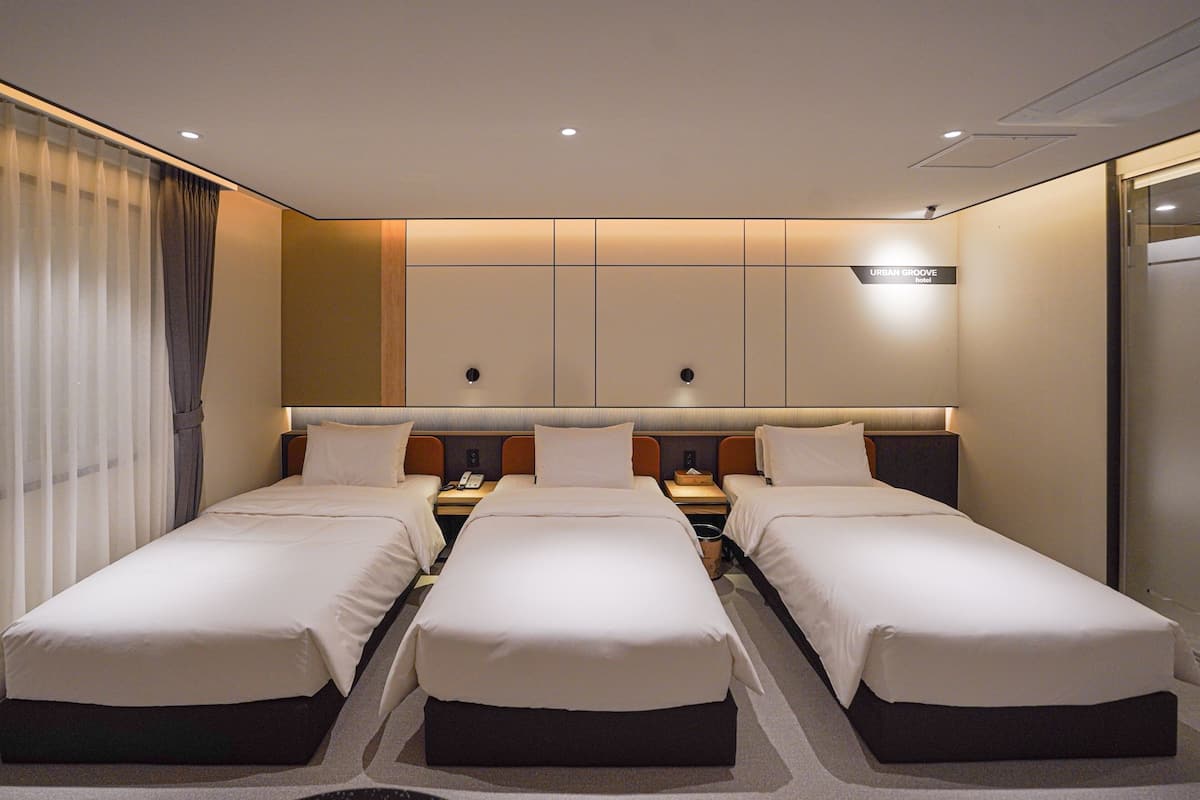 A hotel room with three single beds, a large mirror, and a flat-screen TV.