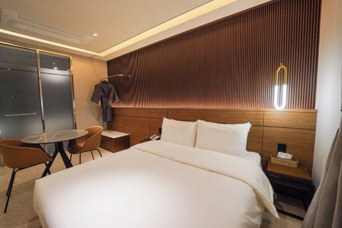 A hotel room with a large bed, a small round table, two chairs, a wardrobe, and a mirror.