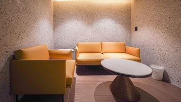 A modern interior with a sofa and armchair, a round table, and a trash bin.