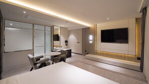 A modern hotel room with a large bed, a desk with a chair, a small table, and a large TV mounted on the wall. - Urban Groove Hotel (Busan)