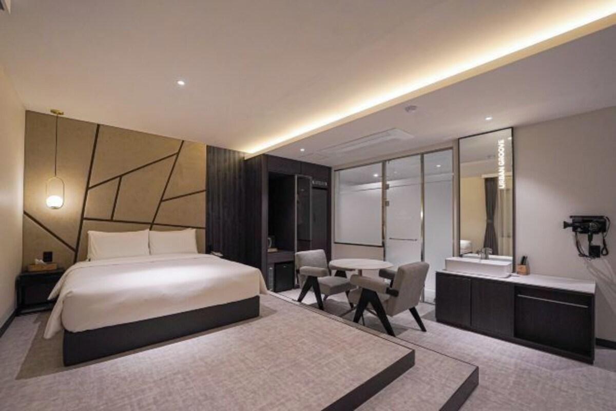 A modern hotel room with a large bed, a desk, and a vanity with a mirror.