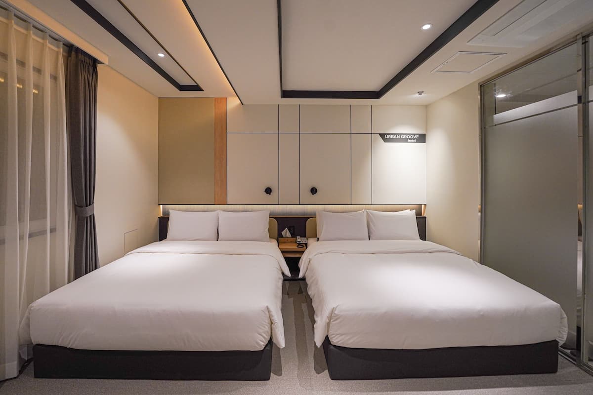 A hotel room with two beds, a nightstand, a wall-mounted TV, and a sliding door.