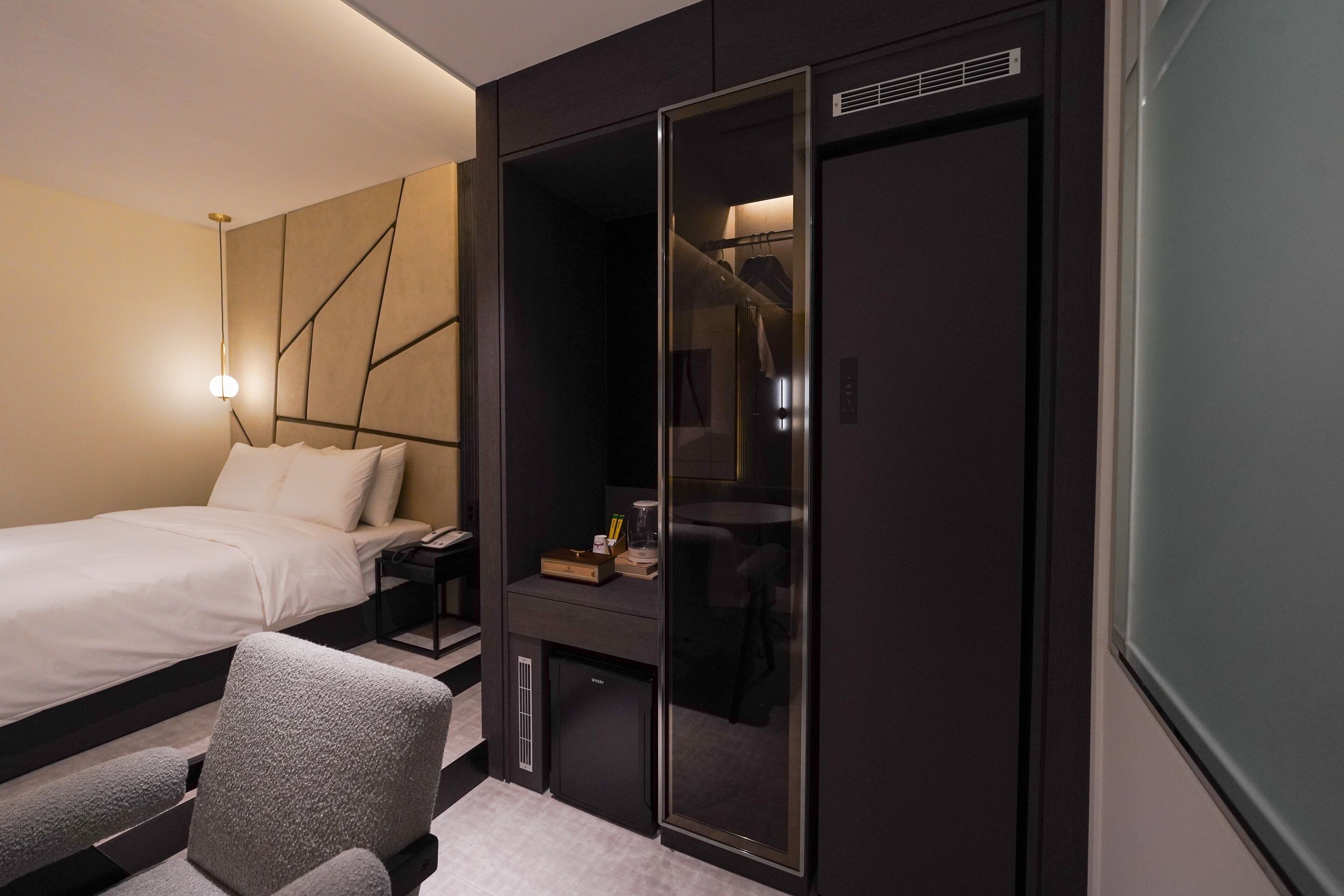 A modern hotel room with a bed, a desk, a wardrobe, and a seating area.