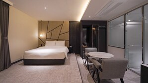 A modern hotel room with a large bed, a small table with two chairs, and a glass partition wall. - Urban Groove Hotel (Busan)