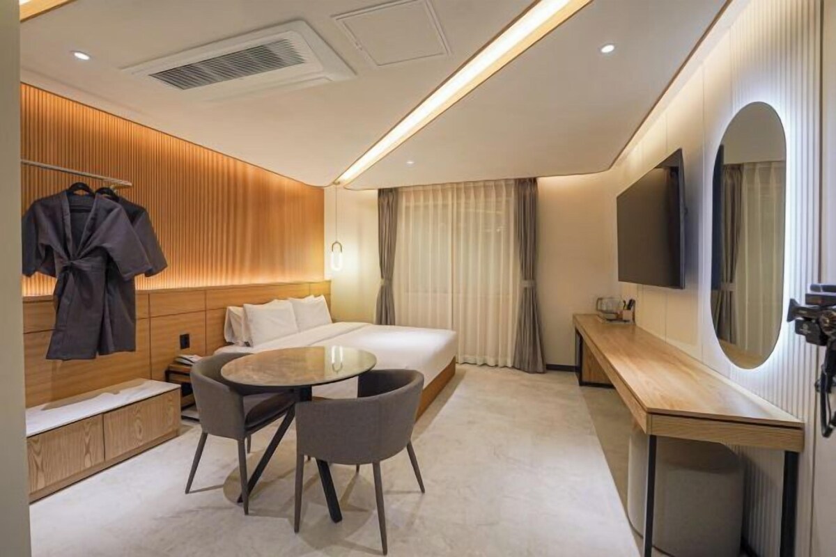 A modern hotel room with a bed, bedside table, chair, and a large mirror.