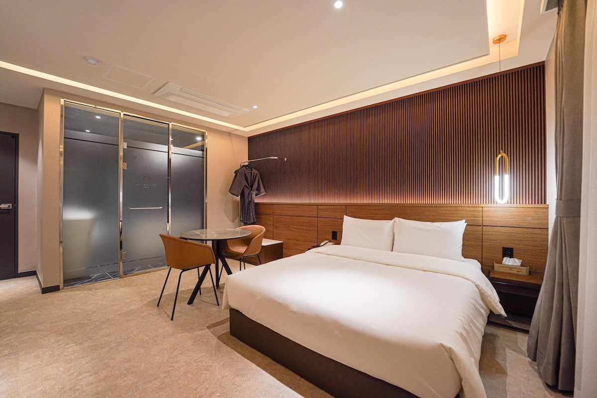 A hotel room with a large bed, a desk with a chair, a coat rack, and a sliding door closet.