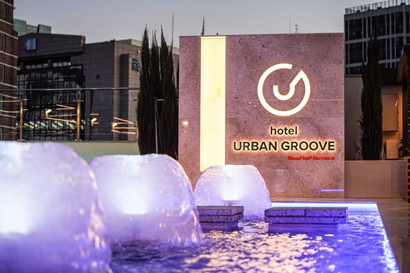 A hotel sign with a modern logo and the name "URBAN GROOVE" on a stone facade, with water features in the foreground. - Urban Groove Hotel (Busan)