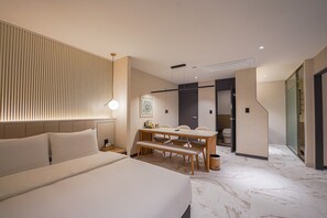 A modern hotel room with a large bed, a dining table with chairs, and a bathroom visible through an open door. - Urban Groove Hotel (Busan)