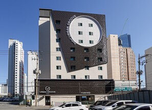 A hotel with a distinctive circular logo on the facade, multiple parking spaces, and a modern urban setting. - Urban Groove Hotel (Busan)