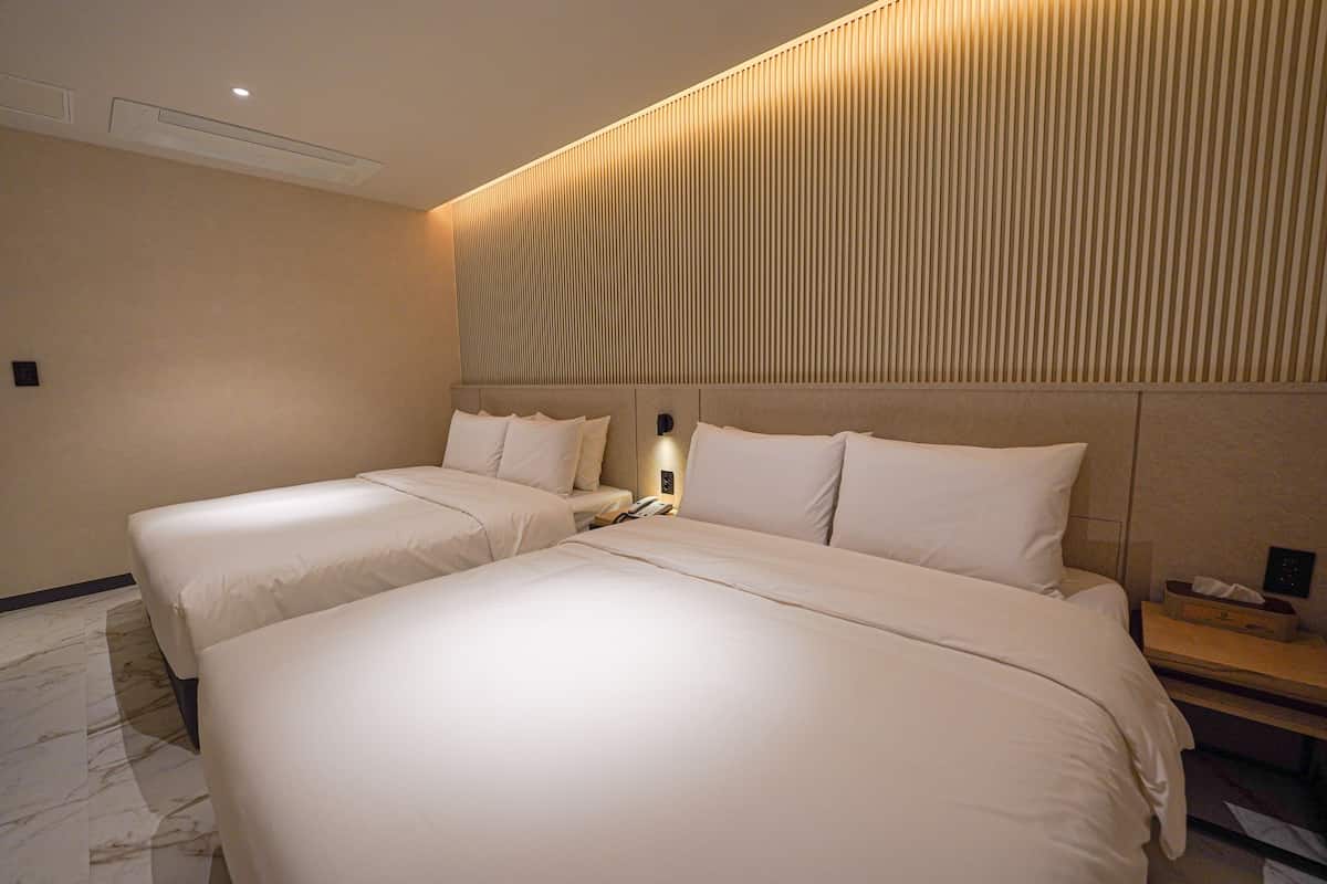 A hotel room with two beds, a nightstand, and a wall-mounted light fixture.