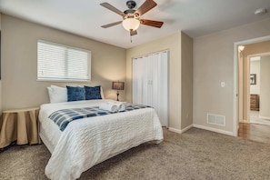 A bedroom with a bed, a ceiling fan, a window with blinds, a bedside table, and a closet.