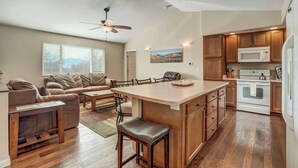 A spacious living area with a large island, a kitchen with wooden cabinets and appliances, and a ceiling fan. - Crestview Place! 2 Mins to UCCS, Patio, and BBQ (Colorado Springs)