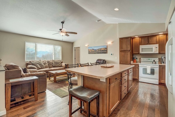 A spacious living area with a large island, a kitchen with wooden cabinets and appliances, and a ceiling fan.