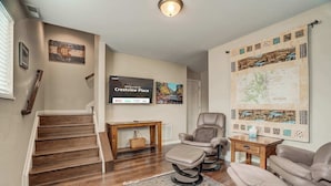 A living room with a wooden staircase, a television, a recliner, a coffee table, and a large map on the wall. - Crestview Place! 2 Mins to UCCS, Patio, and BBQ (Colorado Springs)