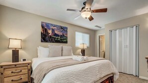 A bedroom with a bed, two bedside tables, a ceiling fan, a painting, a window with blinds, and a closet. - Crestview Place! 2 Mins to UCCS, Patio, and BBQ (Colorado Springs)
