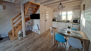 A modern kitchen with white cabinets, a dining area with a wooden table and blue chairs, and a wooden staircase. - Comfortable Holiday Homes for 6 People, Niechorze (Rewal)