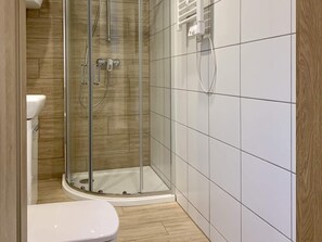 Ein Badezimmer mit Duschkabine, weißer Toilette und gefliesten Wänden.
