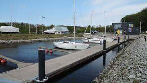 Ein Yachthafen mit anlegenden Booten, ein kleines Gebäude und eine Anlegestelle, die sich ins ruhige Wasser erstreckt.