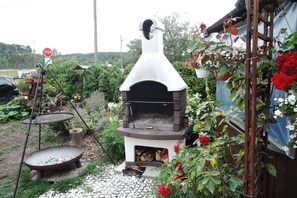 Ein rustikaler Pizzaofen im Freien mit Schornstein, umgeben von einem Garten mit verschiedenen Pflanzen und Blumen.