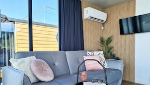 Een moderne woonkamer met een grijze bank, een klein zwart bijzettafeltje en een wandairconditioner.